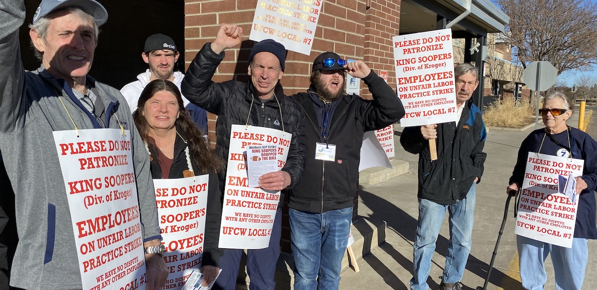 Eight workers hold white and orange strike signs--some have fists in the air and are smiling