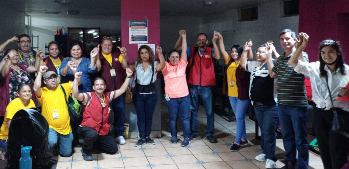 Mexican workers with La Liga gathered indoors in a line with their hands linked and raised in the air