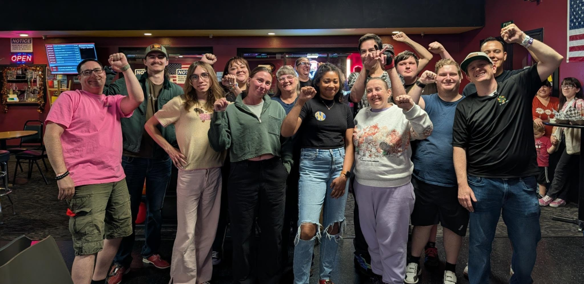 About 15 members of UFCW Local 8 pose for a photo at a bowling alley with their fists raised.