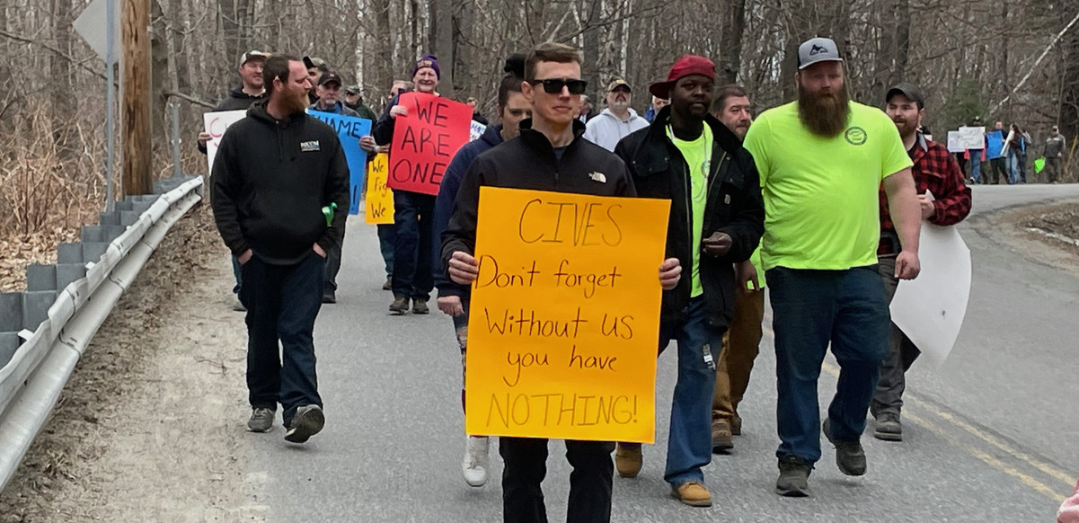 A group of 60, mostly men, a mix of races, marches toward the camera with signs that say “We are One” and “Cives don’t forget without us you have nothing”