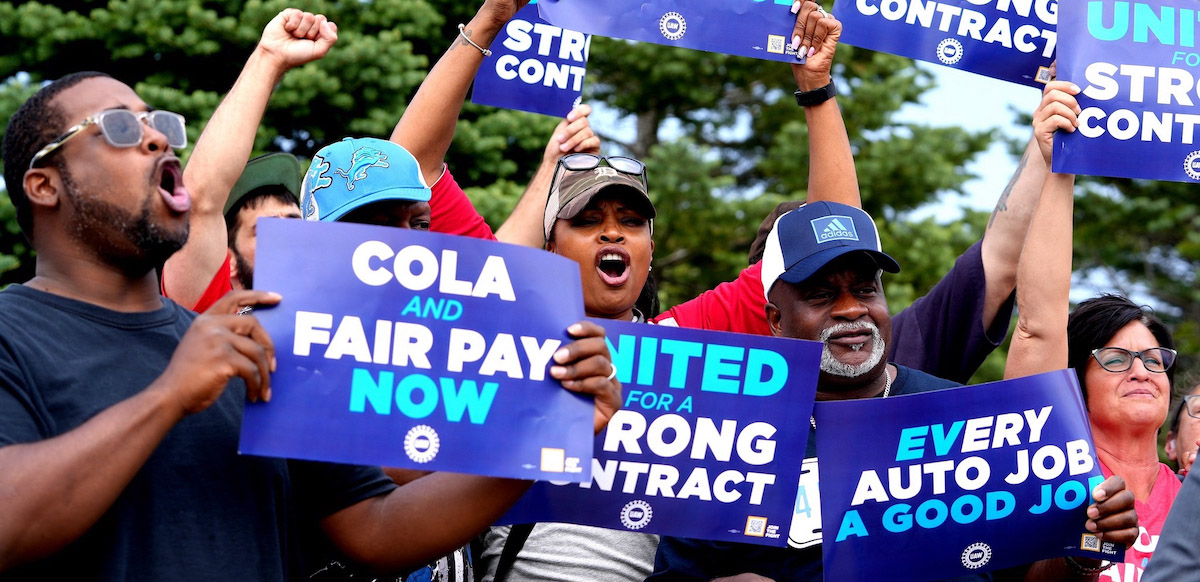 An excited group of six, mostly African American, hold up fists and blue UAW contract campaign signs.