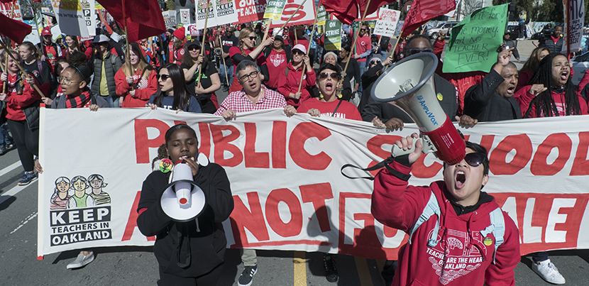 Oakland teachers marching down the street en masse with two bullhorns and a sign.