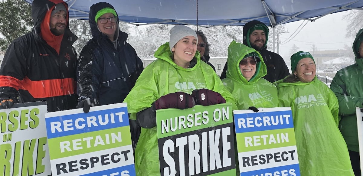 Six smiling people with green and blue strike signs stand under a tent in the snow.