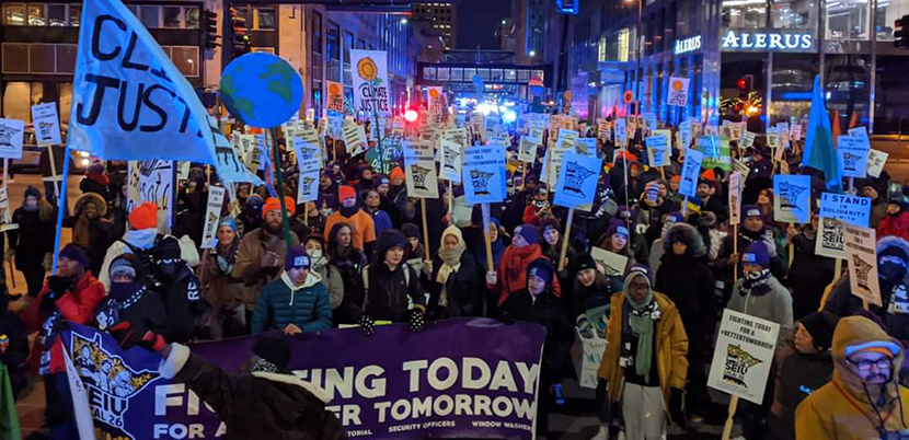 Crowd of climate strikers at night with signs and flags and a banner in downtown Minneapolis.