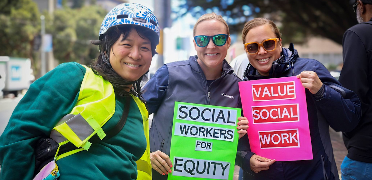 Three women hold signs saying “Social Wokrers for Equity” and “Value Social Work”