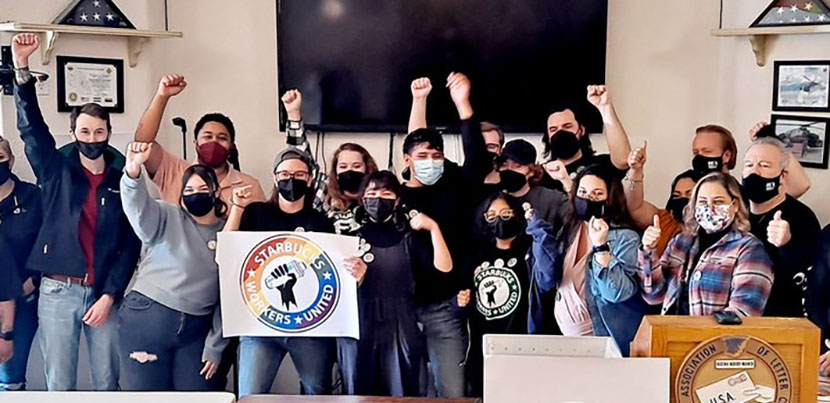 A crowd of Starbucks workers and other Workers United members celebrate with arms raised, posing for photo