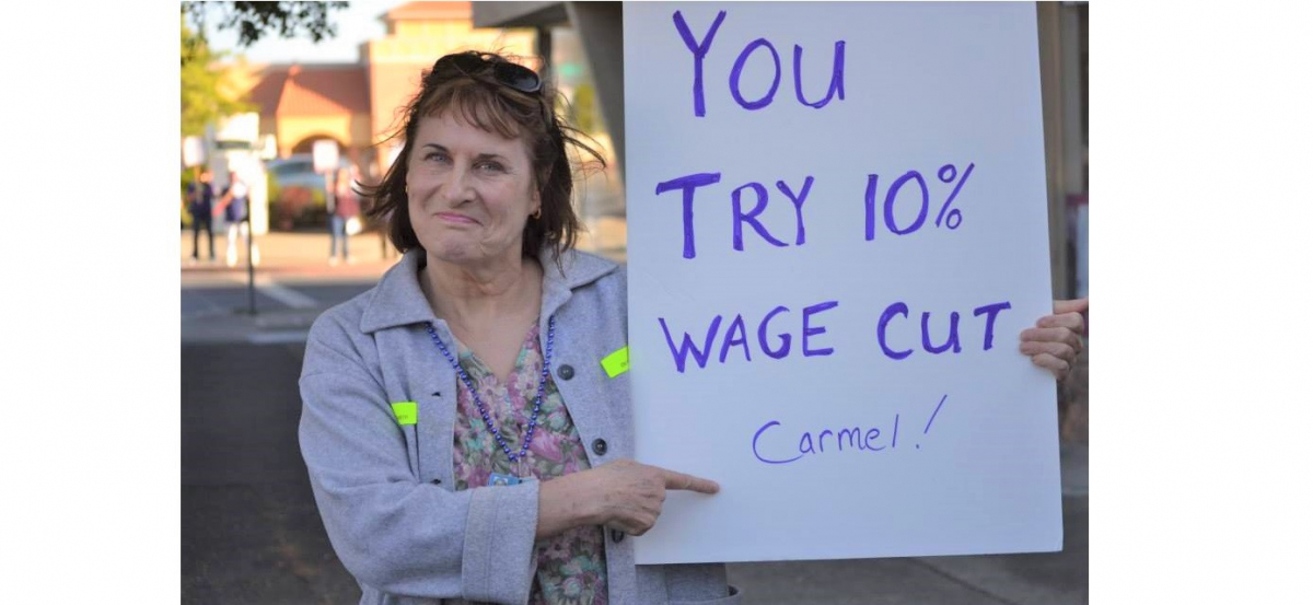 woman outdoors holds sign: "You try 10% wage cut Carmel!"