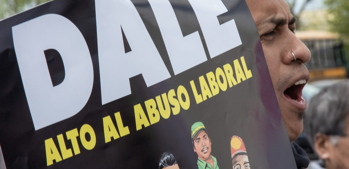 Un hombre grita mientras sostiene un cartel que dice DALE Alto Al Abuso Laboral