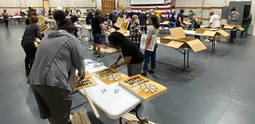 IATSE preparing picketing signs on tables in rows in room with gray floor.