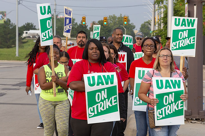 GM strikers march with "UAW on strike" signs. Black and white women in foreground.