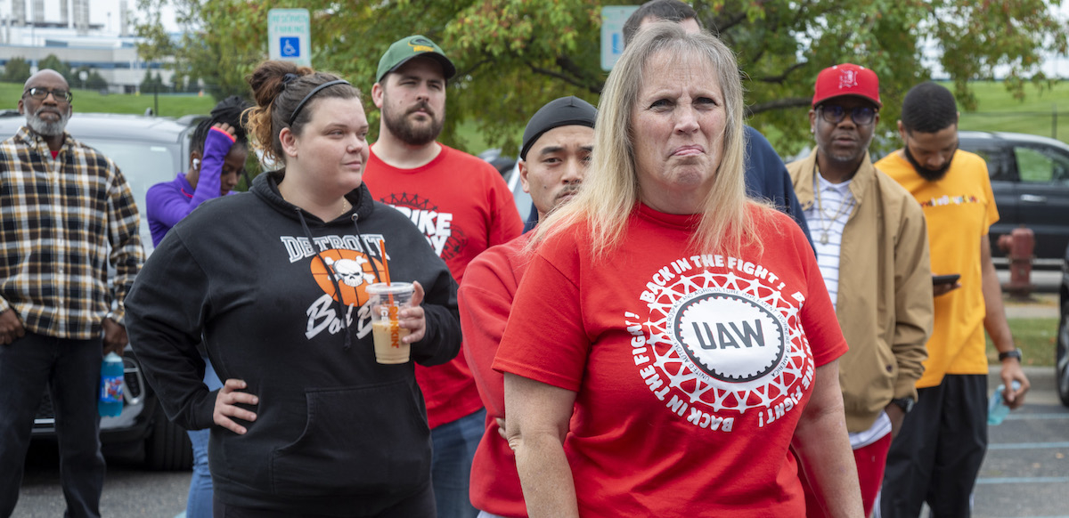 A determined-looking woman with a crowd behind her wears a red shirt saying UAW, Back in the Fight