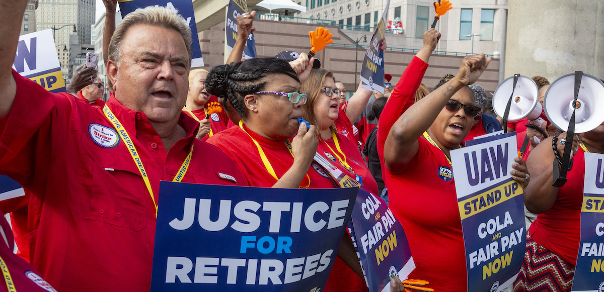 Auto workers in red shirts hold signs, including “justice for retirees”