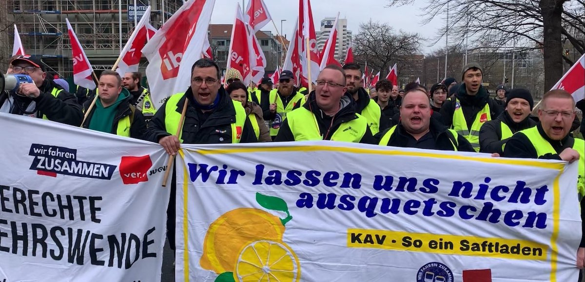 People with red flags march behind a banner adorned with lemons.