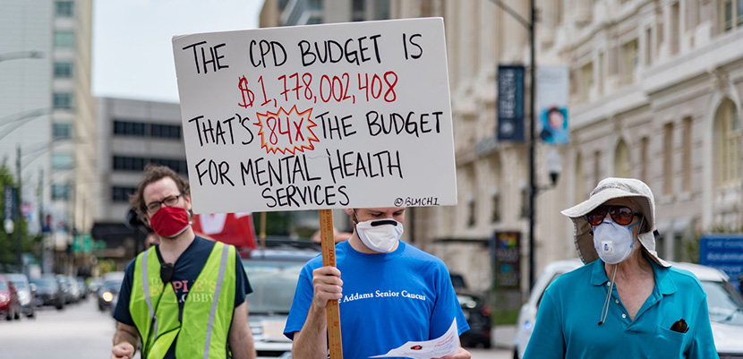 Three people marching against police brutality and for health care in Chicago with a sign