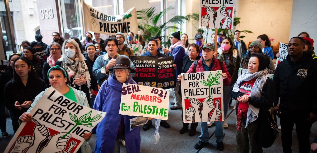 A group of forty cram into a building lobby with signs saying “Labor for Palestine”