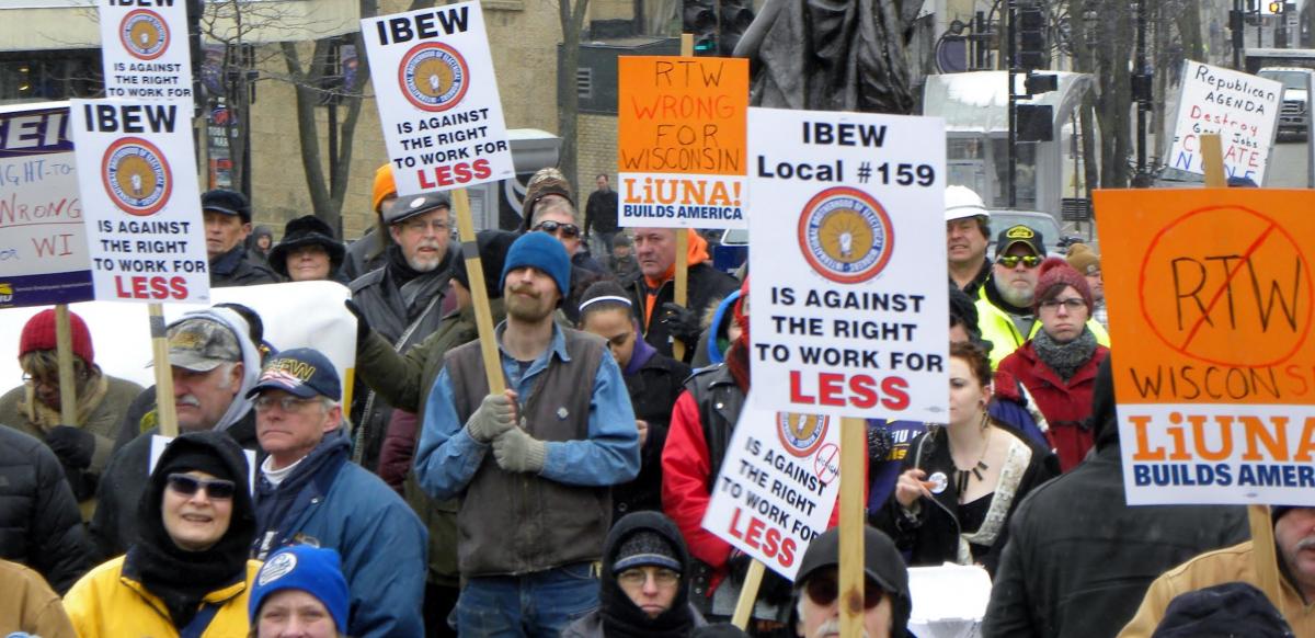 Warmly dressed people march with LIUNA and IBEW union signs opposing "Right to work for less" in Wisconsin.