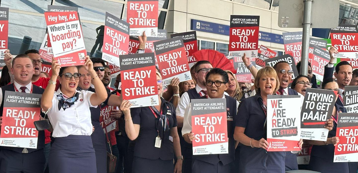 Dozens of men and women of various ethnicities wearing dark blue flight attendant uniforms hold signs saying “Ready to Strike”