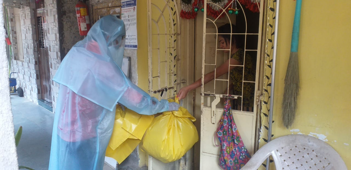 Dalit sanitation worker in a PPE suit accepting trash in yellow bags by hand from the home of a coronavirus patient