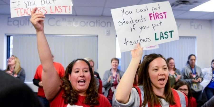 Two teachers holding signs. Tiffany's sign says "You can't put students first if you put teachers last."