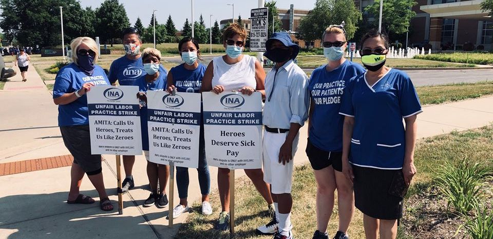 Nurses hold picket signs that read "AMITA: Calls Us Heroes, Treats Us Like Zeroes," in front of St. Joseph Hospital.