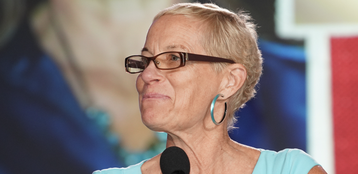 Photo of Jane McAlevey smiling at a microphone and looking left in an aqua blue shirt