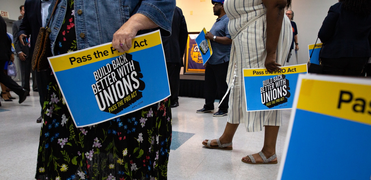 Several woman hold blue and yellow signs that read "Pass the Pro Act: Build Back Better with Unions."