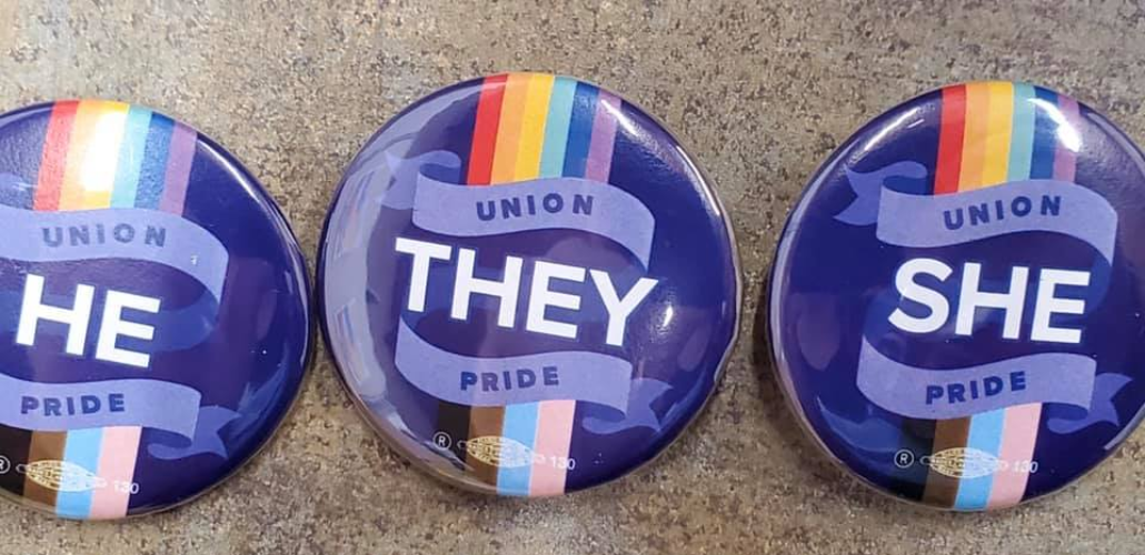 Three purple buttons. Pronoun "He," "They," or "She" is surrounded on each button by rainbow flag, trans flag, and the words "Union Pride."