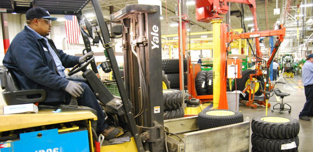 A worker drives a forklift inside a John Deere plant