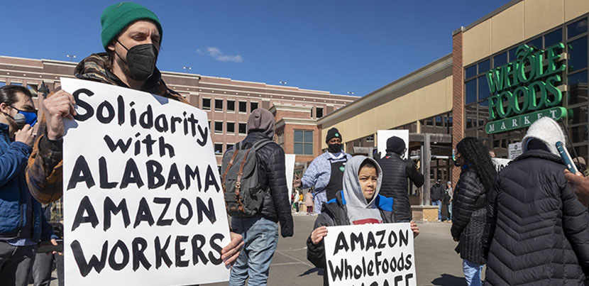 Adult and boy with signs in front of Whole Foods supporting Alabama Amazon workers attempting to unionize.