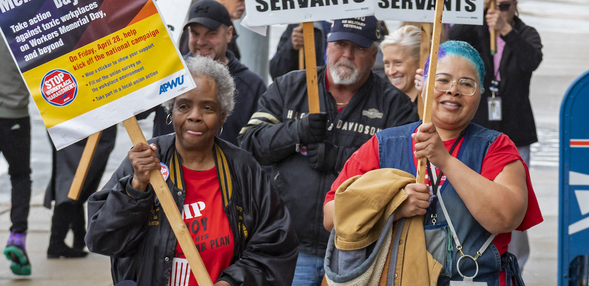 Postal workers march with signs about working conditions.