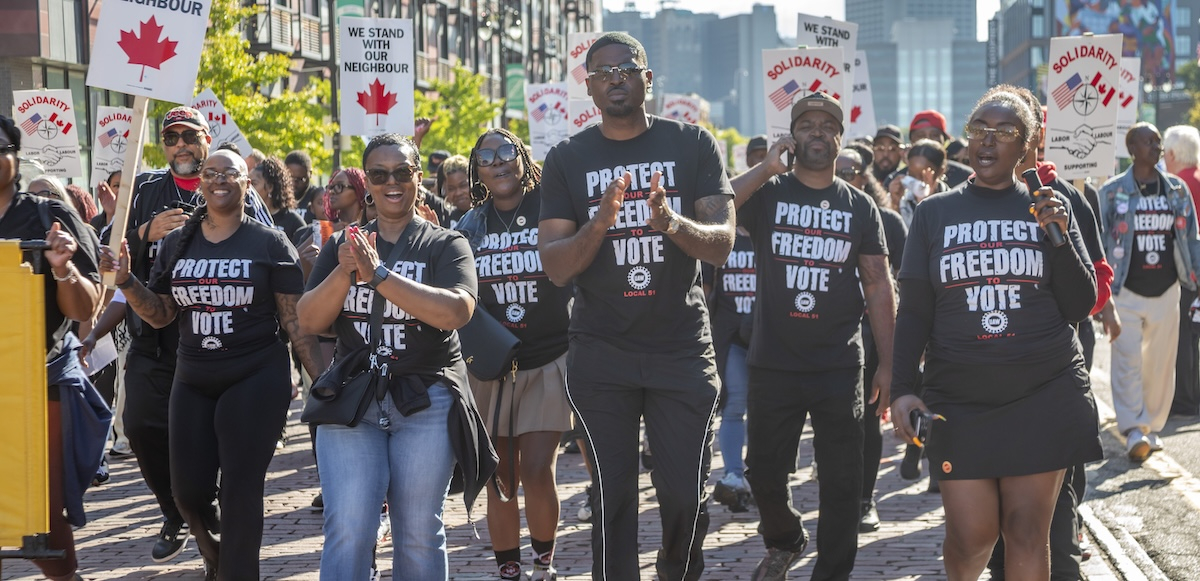 A group of autoworkers with black “Protect Our Freedom to Vote” shirts march