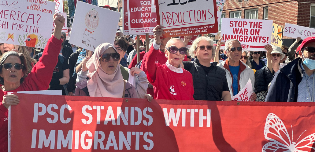 Workers, mostly women, carry a big red banner with white letters: "PSC stands with immigrants." They are in a big crowd. Some also carry picket signs, some printed and some handwritten, with messages (some partially visible) including "Dictators don't belong here," "America? Fight for it!" "Oranges don't belong in the White House," "Stop the war on immigrants," and "Stop the coup." One woman wears a hijab.