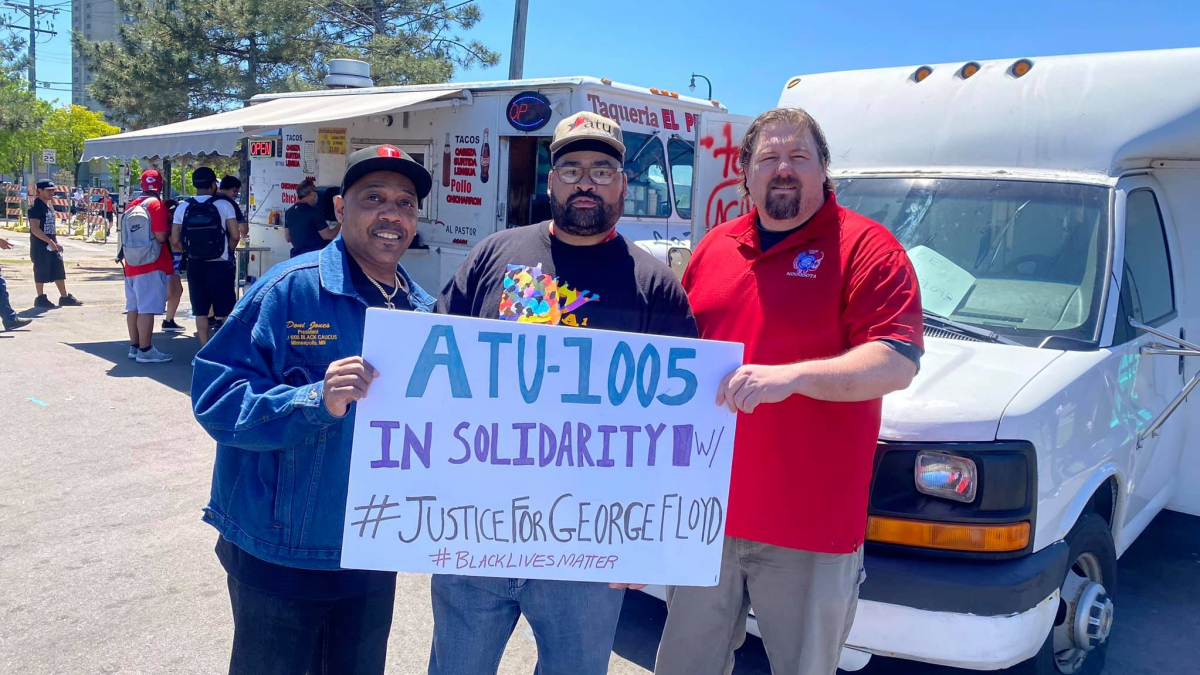 Three men (two Black, one white) hold a sign: "ATU-1005 in solidarity w/ #JusticeForGeorgeFloyd #BlackLivesMatter." Taco truck in background.