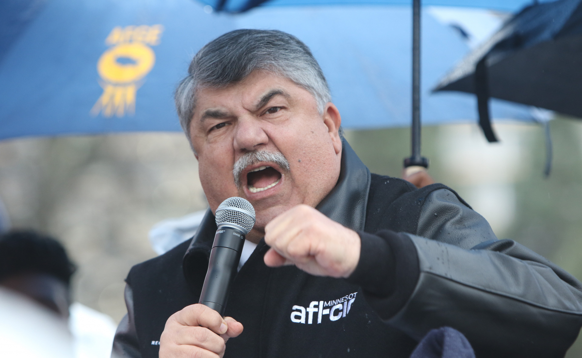 Richard Trumka speaking animatedly into a microphone, under an umbrella, at a 2016 demonstration.