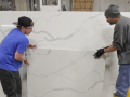 Two workers place a slab of manufactured stone against a larger slab.