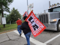 workers cross the road carrying UE flags in front of a grey semi tractor-trailer