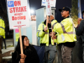 a young asian woman grips a sign that says on On Strike at Boeing. Others around her have signs. It’s nighttime.