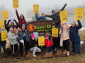 A group of 20 workers in winter clothes gather with yellow UFCW signs around a SuperOne Foods sign