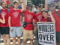 A group of Google workers stand in red shirts behind a sign that reads Workers Over Billionaires.