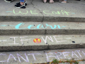 Steps chalked in blue and pink with the words we can't learn if we can't breathe with a few students feet and shoes visible