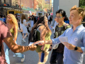 a man in a blue shirt hands a flier to a passerby wearing a backpack