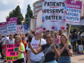 A group of nurses hold picket signs by a street
