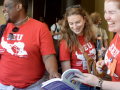 Two women and a man, all wearing Somerville Educators red T-shirts, laugh as they look at a book