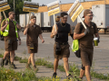 A line of men in brown UPS uniforms and backwards hats with signs saying “Just Practicing for a Just Contract” walk by trailer trucks labeled UPS.