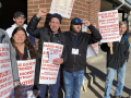Eight workers hold white and orange strike signs--some have fists in the air and are smiling