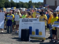 A group of 50 in yellow union shirts rallies in a grocery store parking lot.