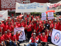 A large crowd of SINTTIA members in red shirts hold banners celebrating May Day