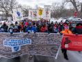 People march in the street on a snowy day. Those at the front carry two huge banners: MFT banner has blue union logo and hundreds of tiny images of members holding signs. SFPE one is red. Others in crowd are holding up beautiful hand-painted signs on sticks with messages like "Educators: the heart of the community" (with a fist/heart image) and "Educators for Black lives"