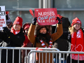 Three smiling nurses stand against a barrier with signs about patient care
