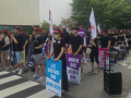Hundreds of workers in black shirts and red headbands stand in rows of six, holding signs and flags.